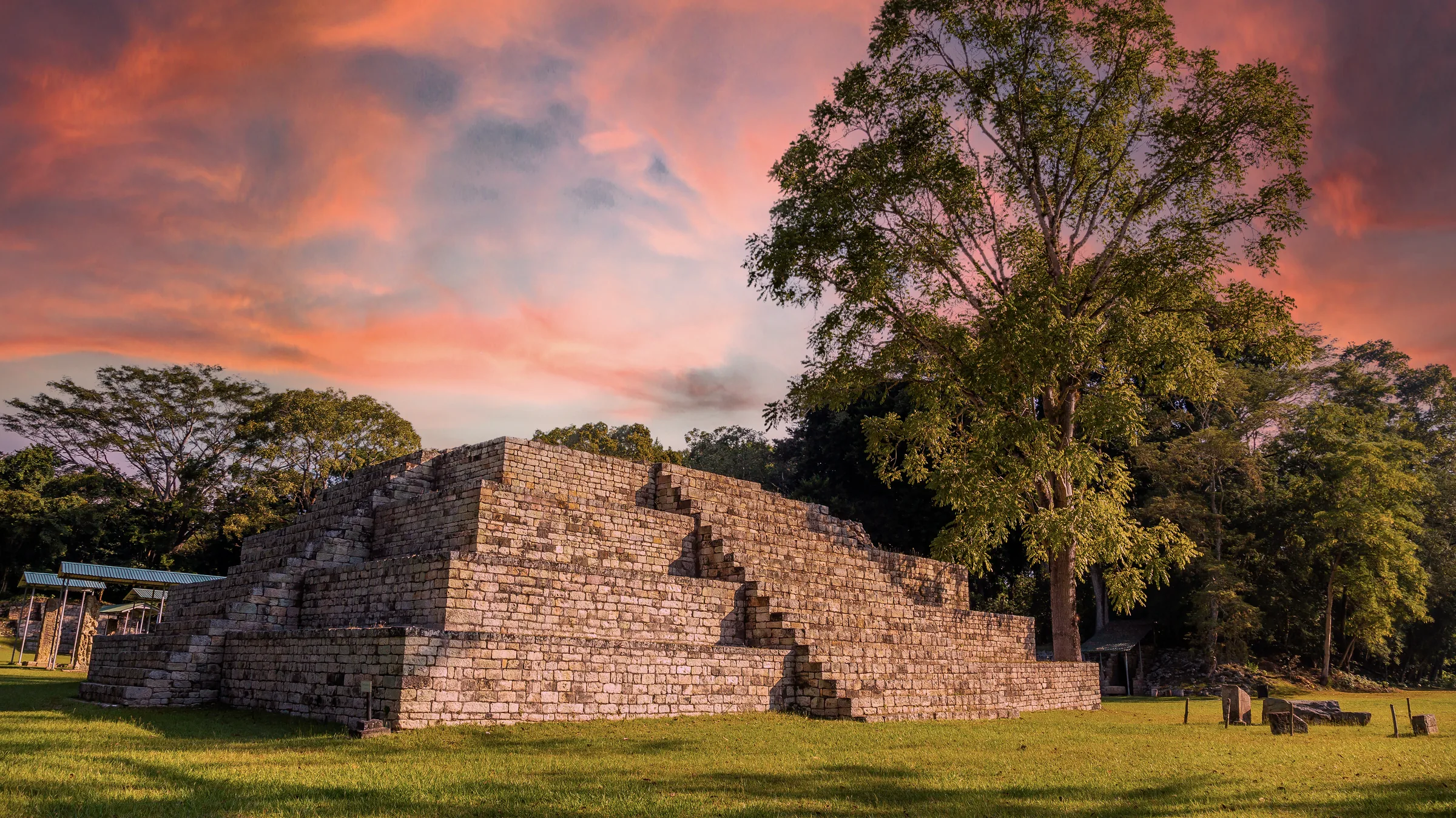 A stepped stone structure at Copán beside trees, beneath an orange sky.