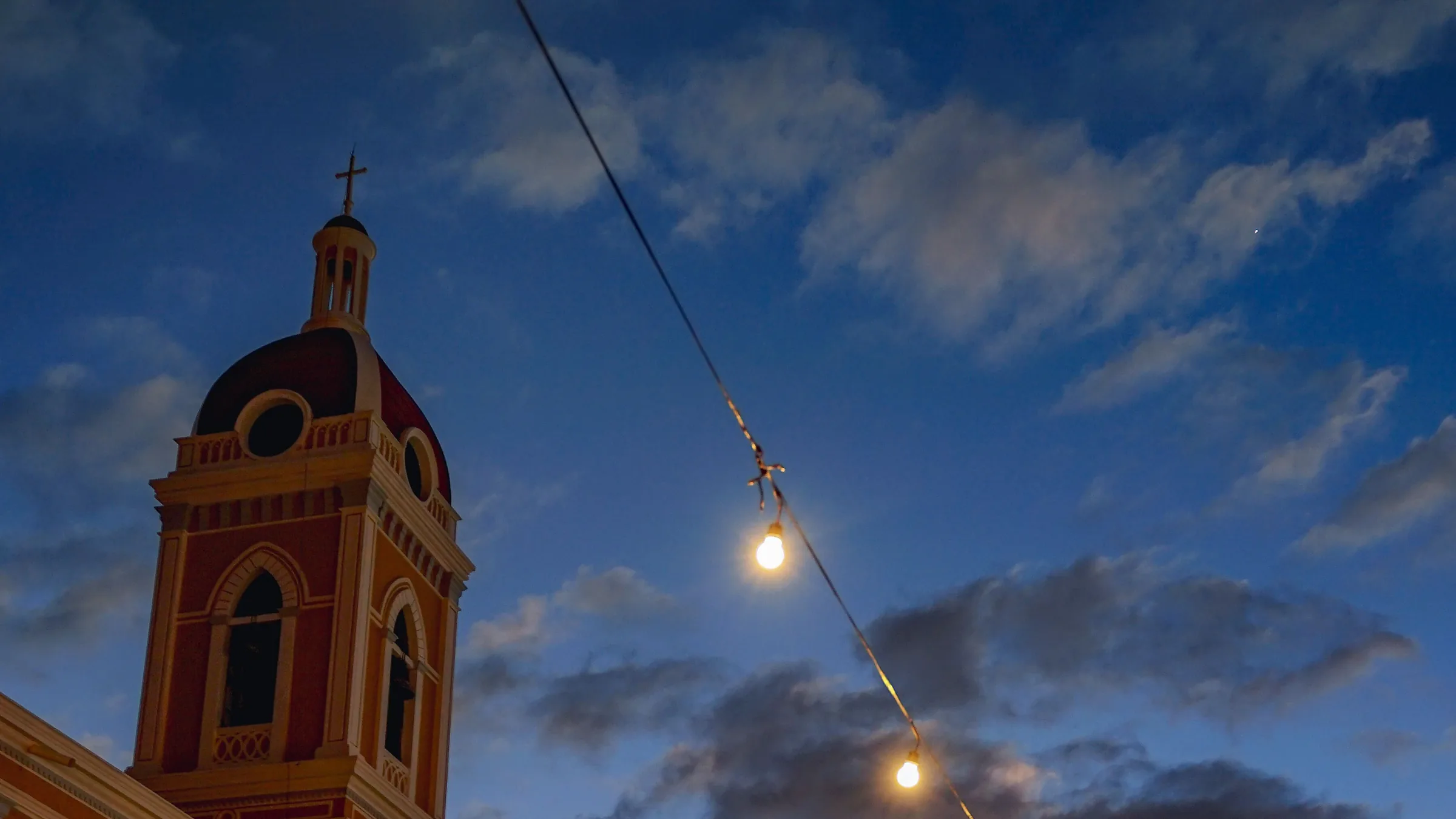 The bell tower of Granada cathedral at dusk, with a string of lights over the square.