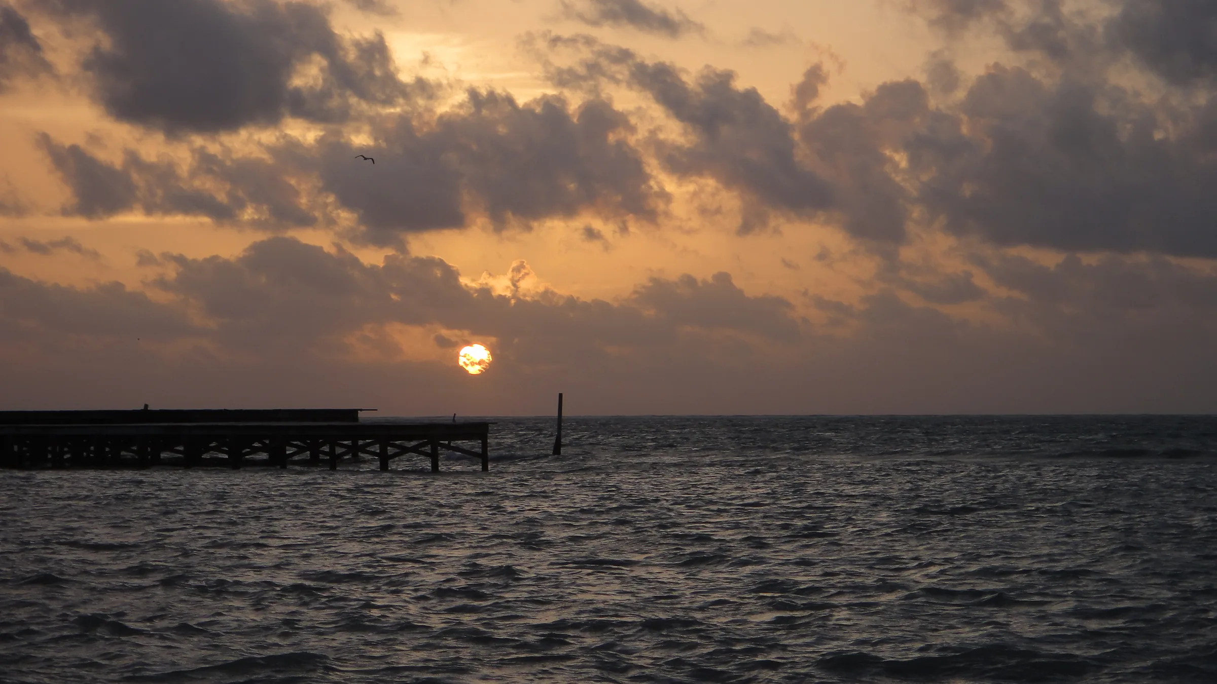 Pier over the sea beneath sunlit clouds in Ambergris Caye.