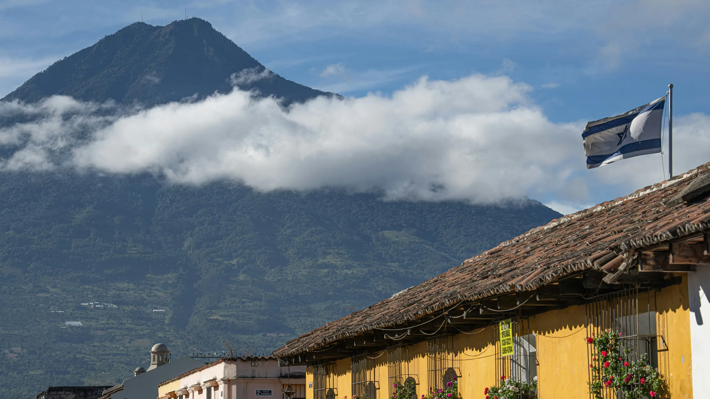 Tiled-roof houses and a volcano among clouds in Antigua Guatemala.