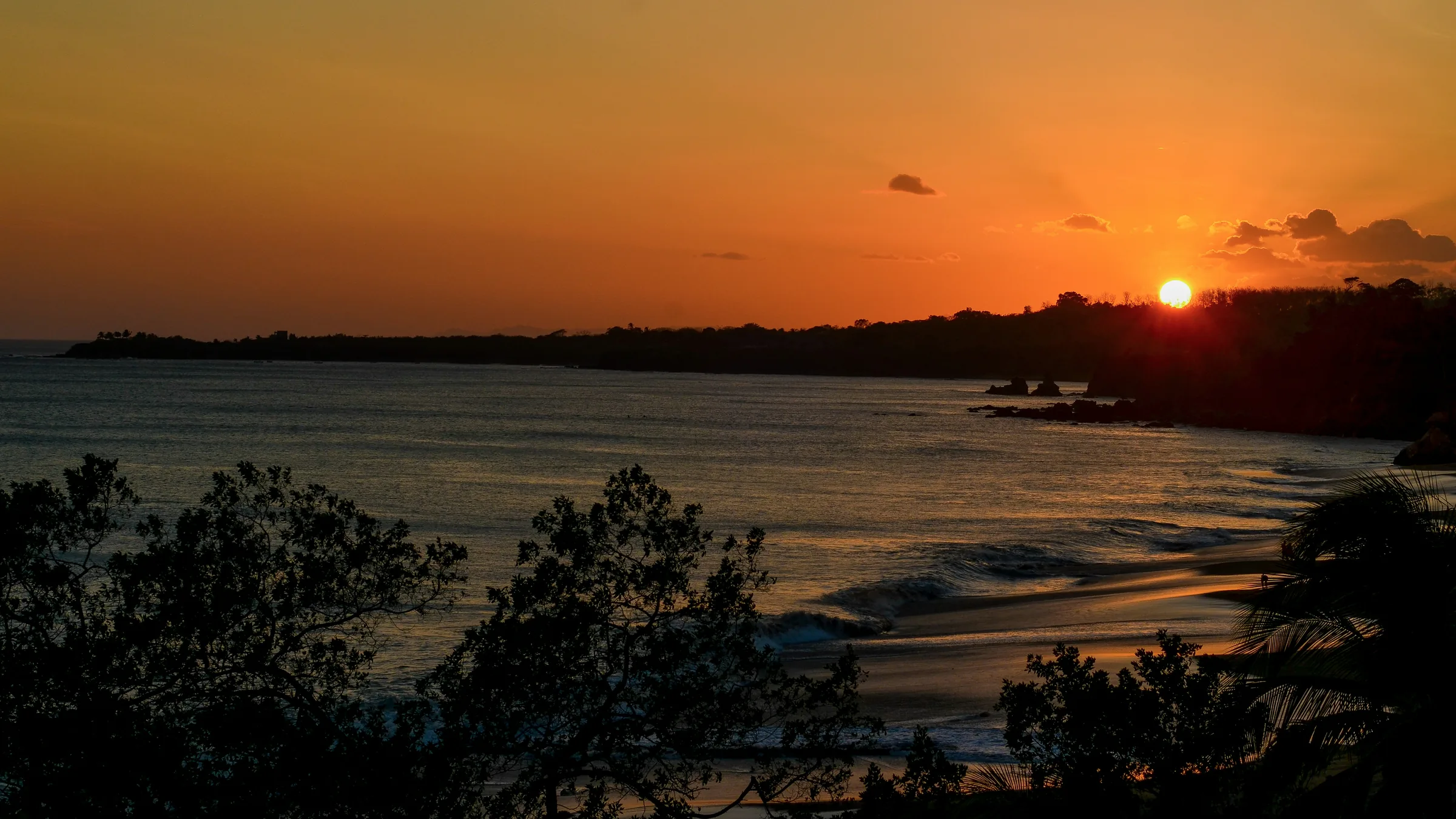 Low sun over a bay, with the coast and vegetation in silhouette.