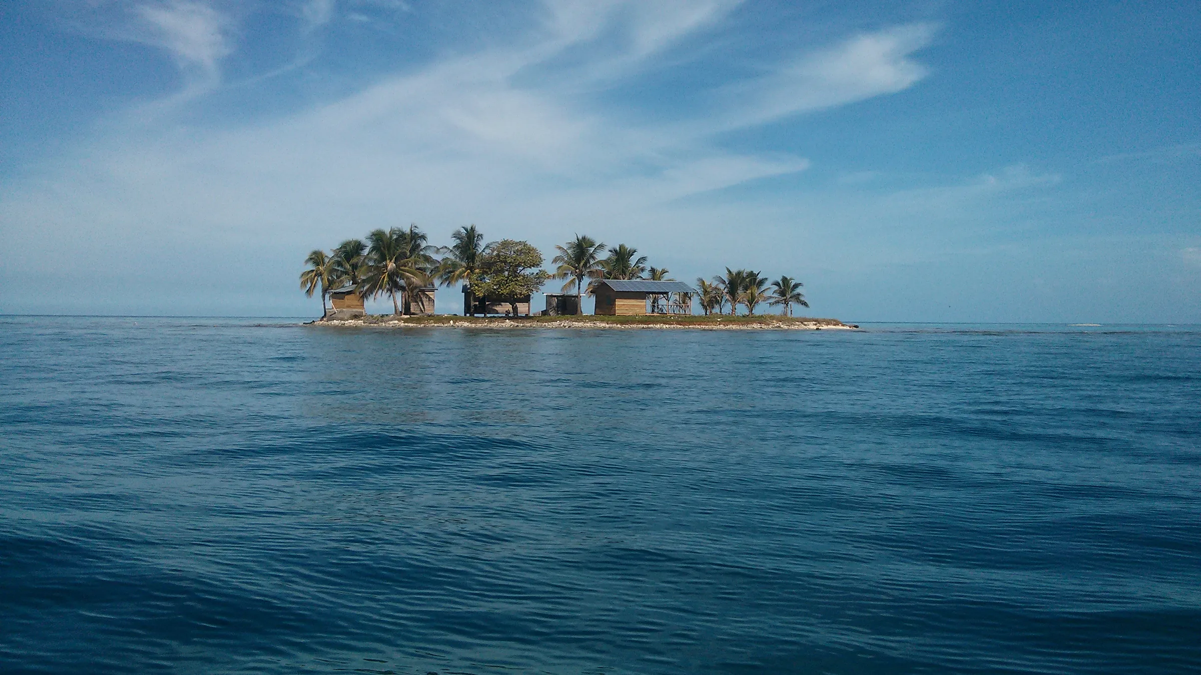 Small cay with palm trees and buildings surrounded by the sea.