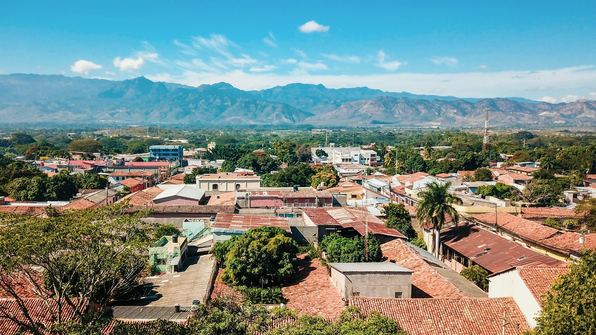 Rooftops and a tree-lined square in Comayagua with mountains behind.