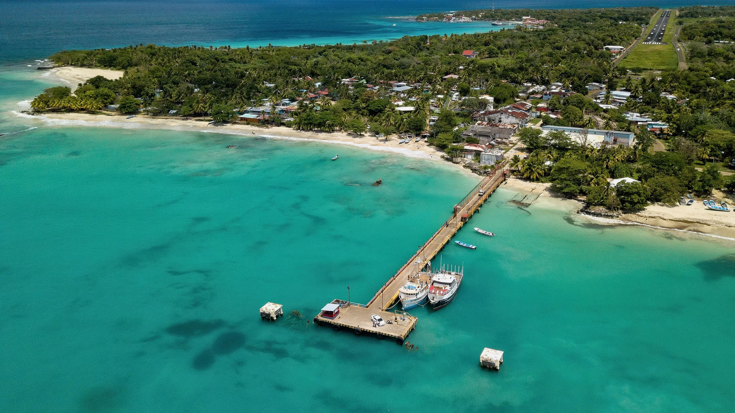 Aerial view of Corn Island with its pier, boats, turquoise water and the town among trees.