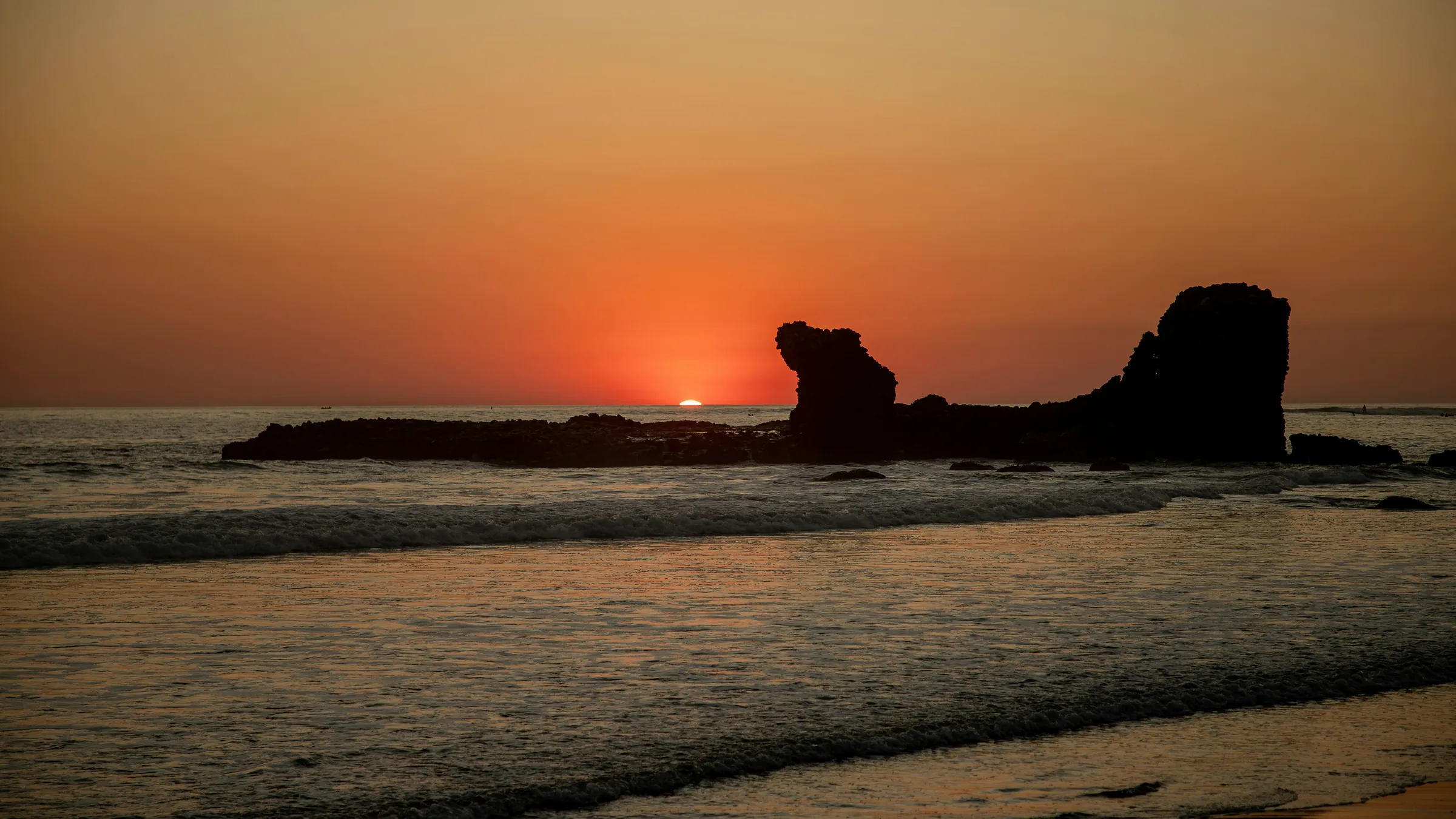 Sun near the horizon and rock formations off El Tunco beach.
