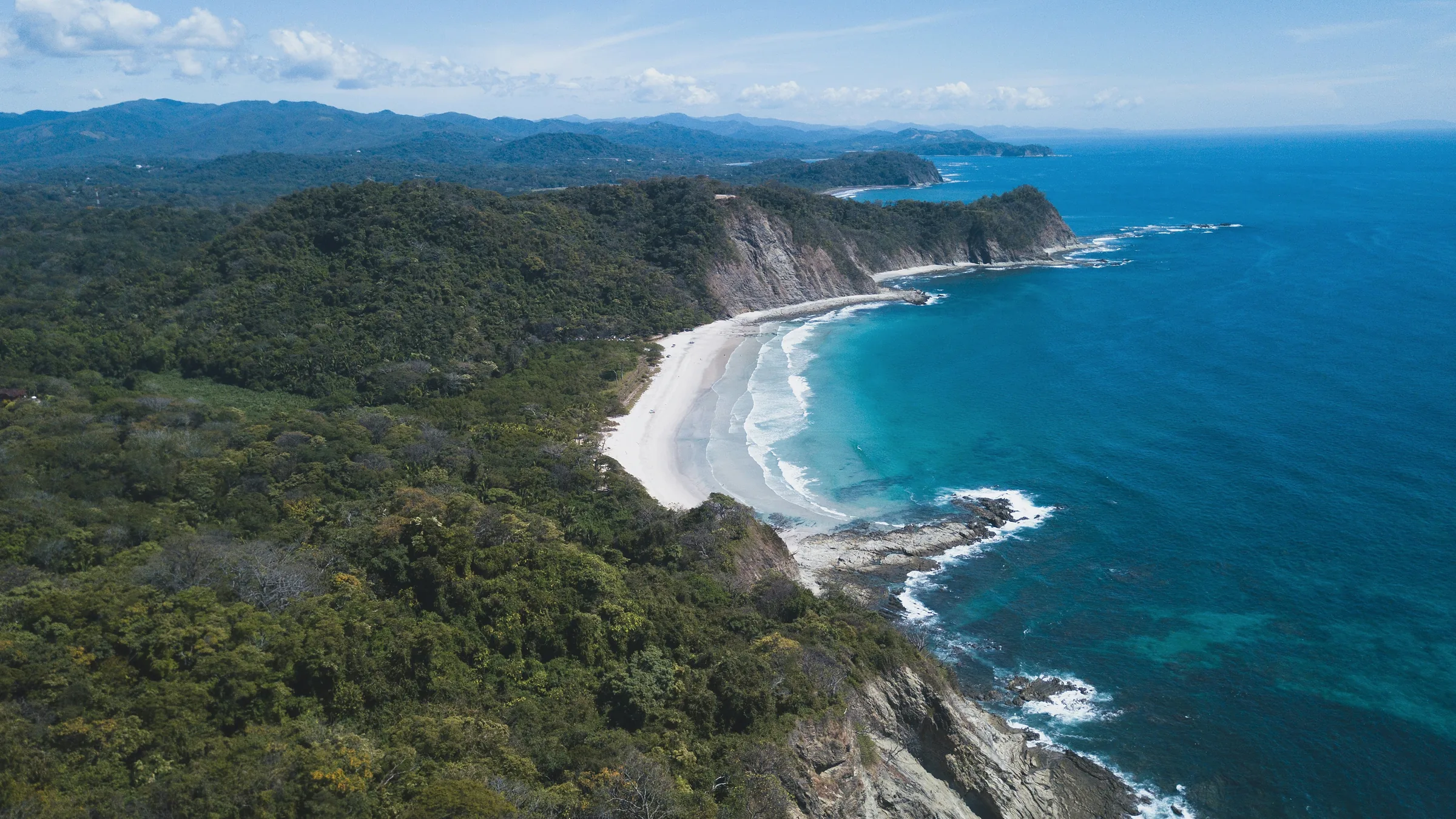 Aerial view of a curved beach below wooded hills in Guanacaste.