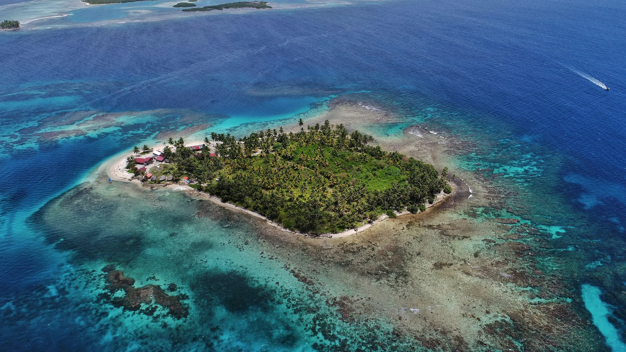 Aerial view of a palm-covered island surrounded by turquoise and deep blue water.
