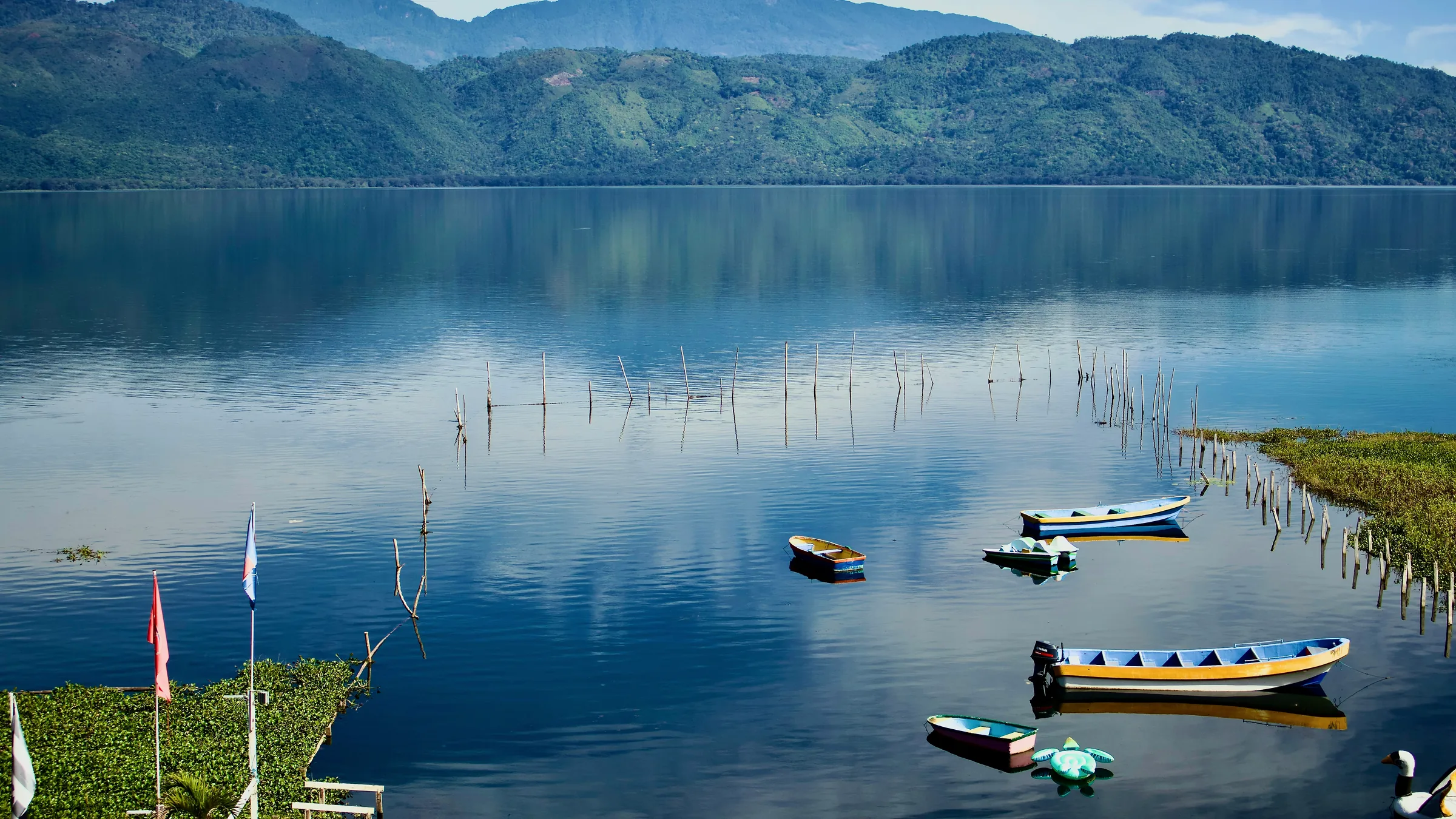 Boats near the shore of Lake Yojoa and mountains reflected in the water.