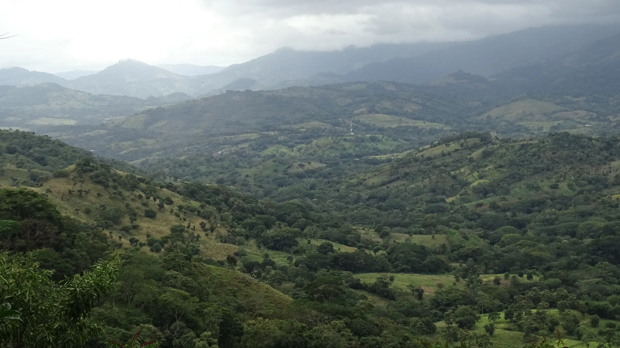 Valley of green hills and mountains beneath low clouds.