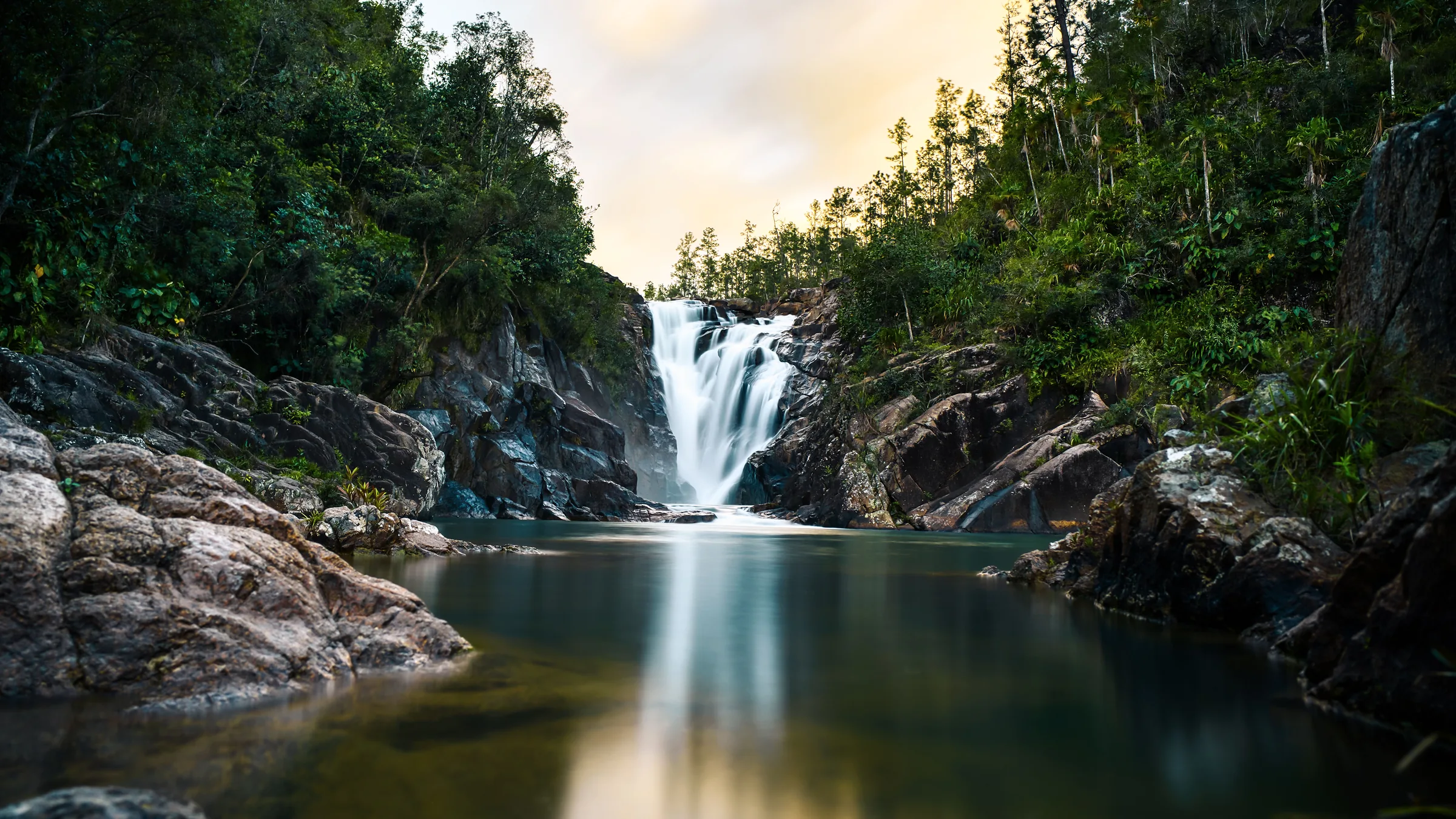 Waterfall between rocks and forest flowing into a pool.