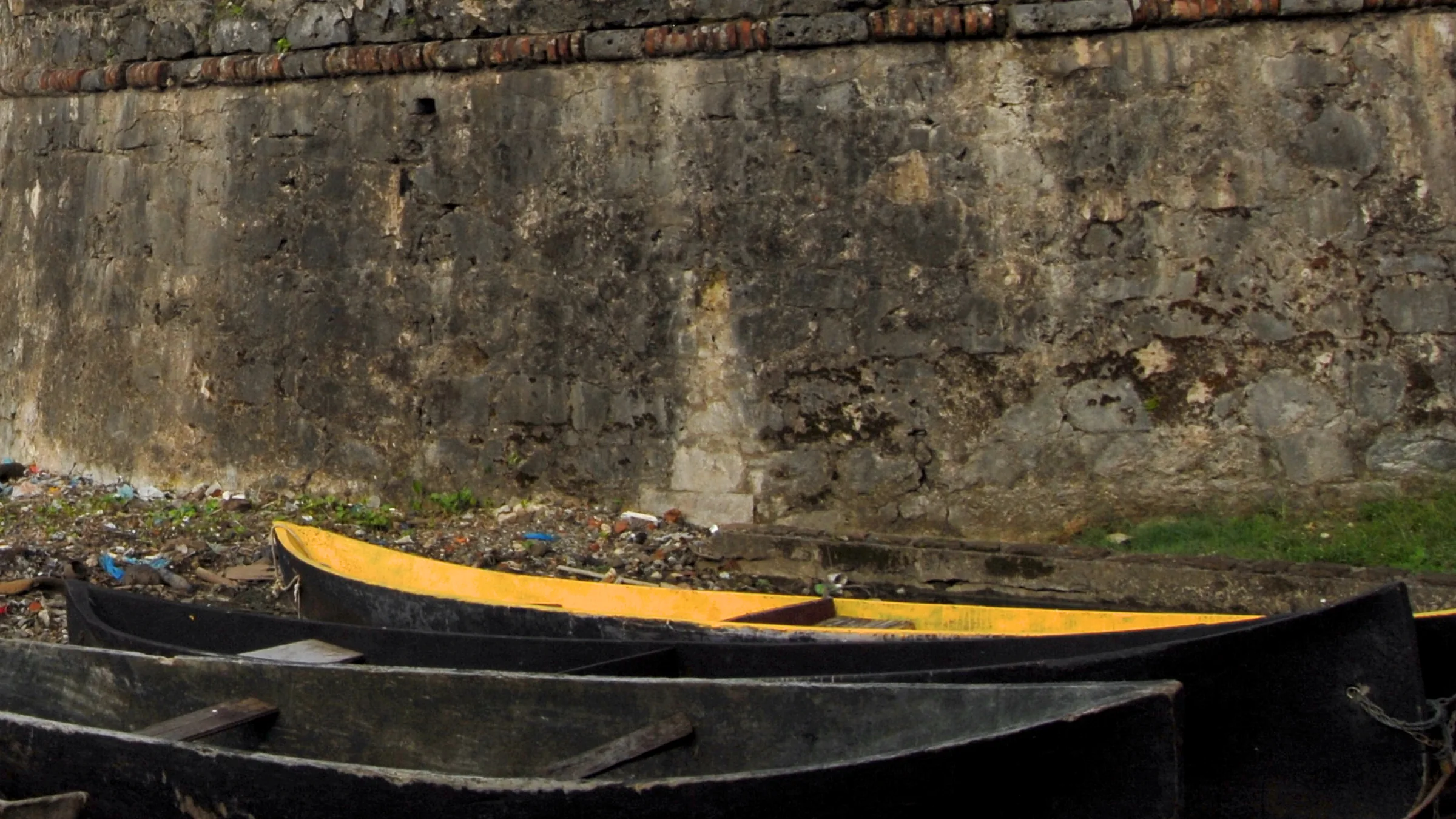 Stone wall of the fort at Portobelo with boats beached in front of it.