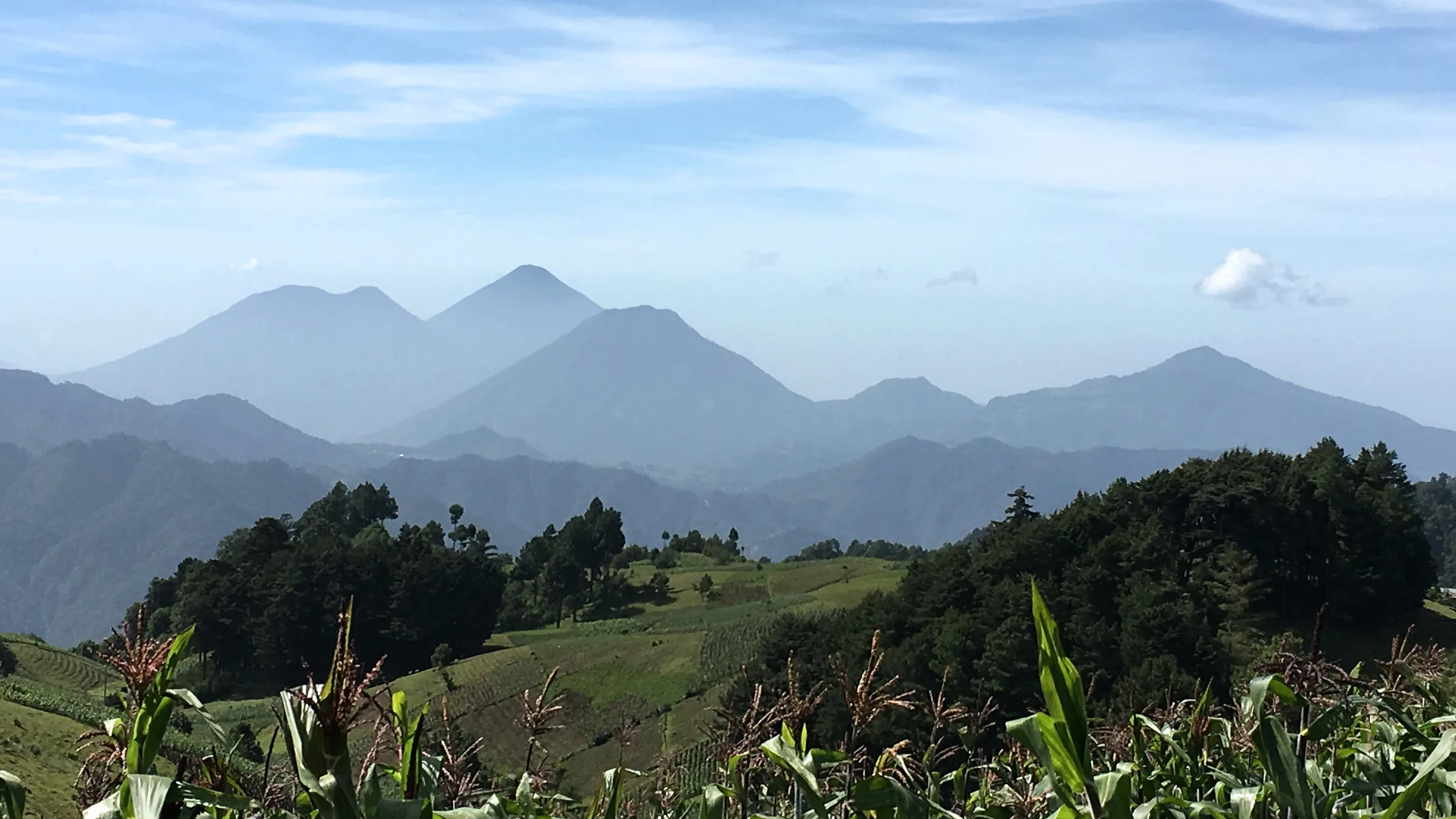 Layers of mountains and a green slope with crops in the foreground.
