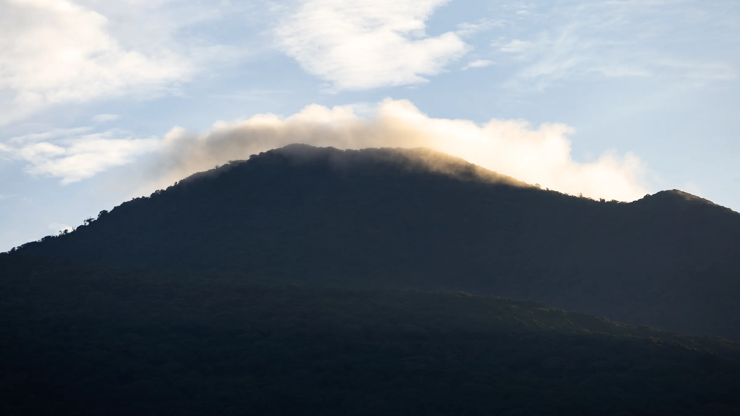 Dark slope of Rincón de la Vieja with clouds around the summit.
