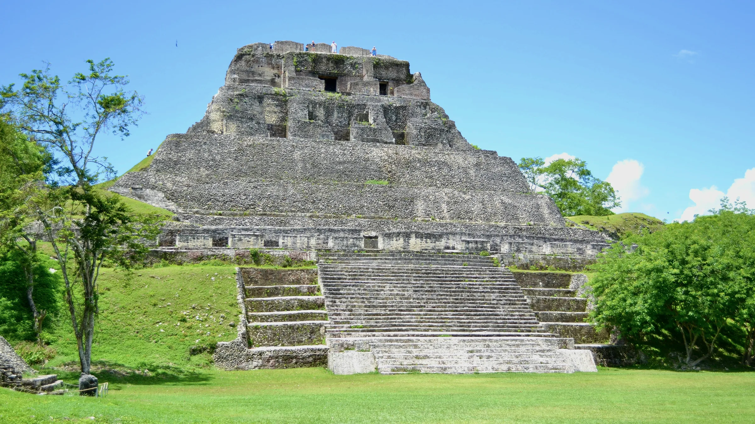 Stepped Maya temple with a central staircase and grass at its base.