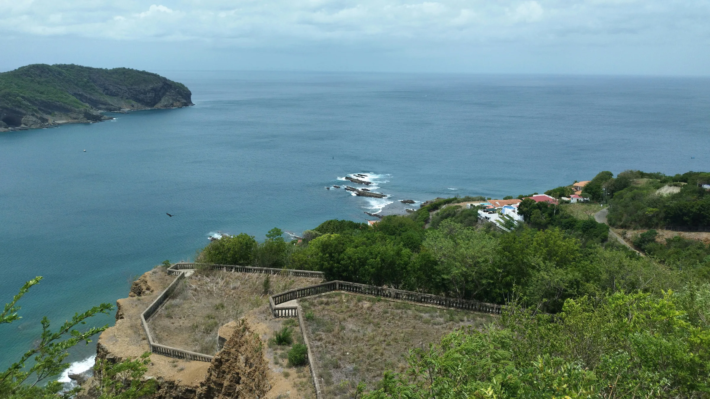 Bay and green coastline seen from a height with stone walls in the foreground.