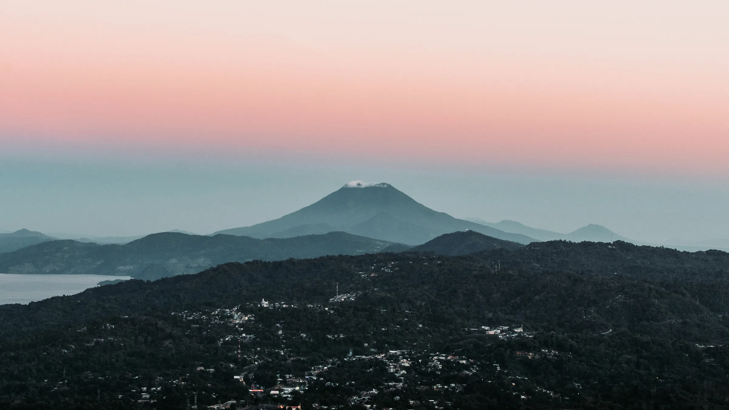View of hills and a distant volcano beneath a pink sky.