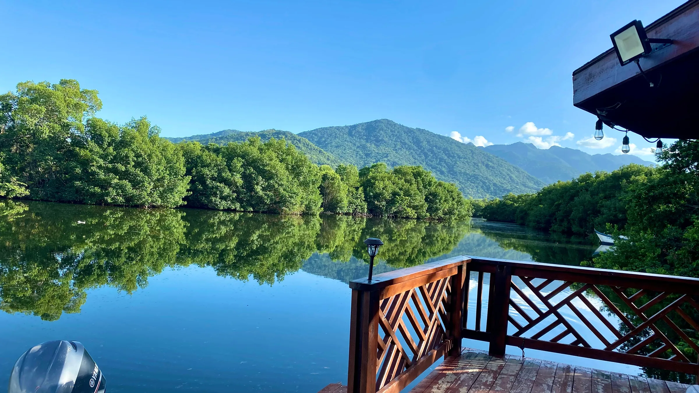 Calm water reflecting trees and mountains, seen beside a wooden railing.
