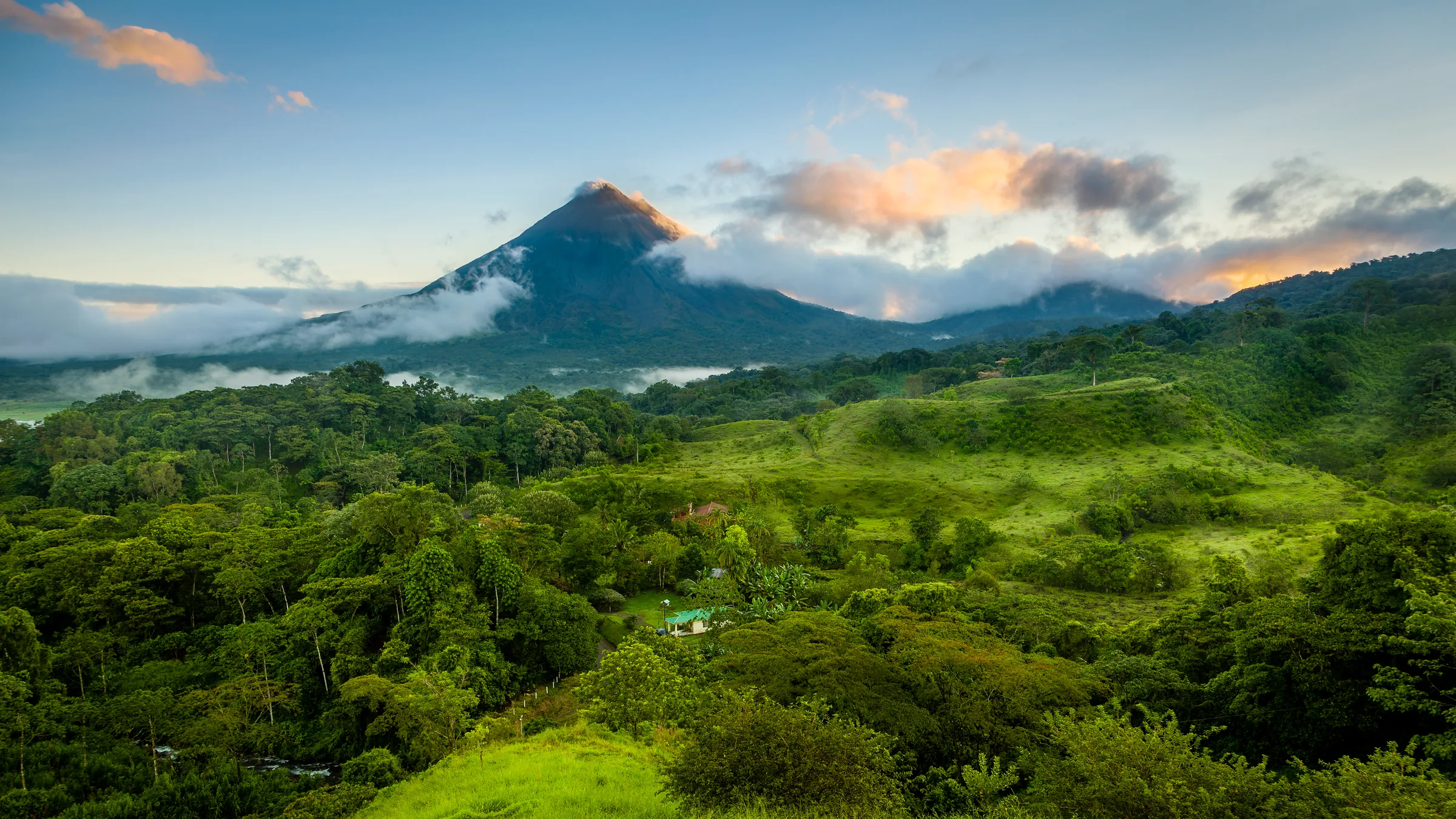 Arenal Volcano among clouds above forest-covered hills.