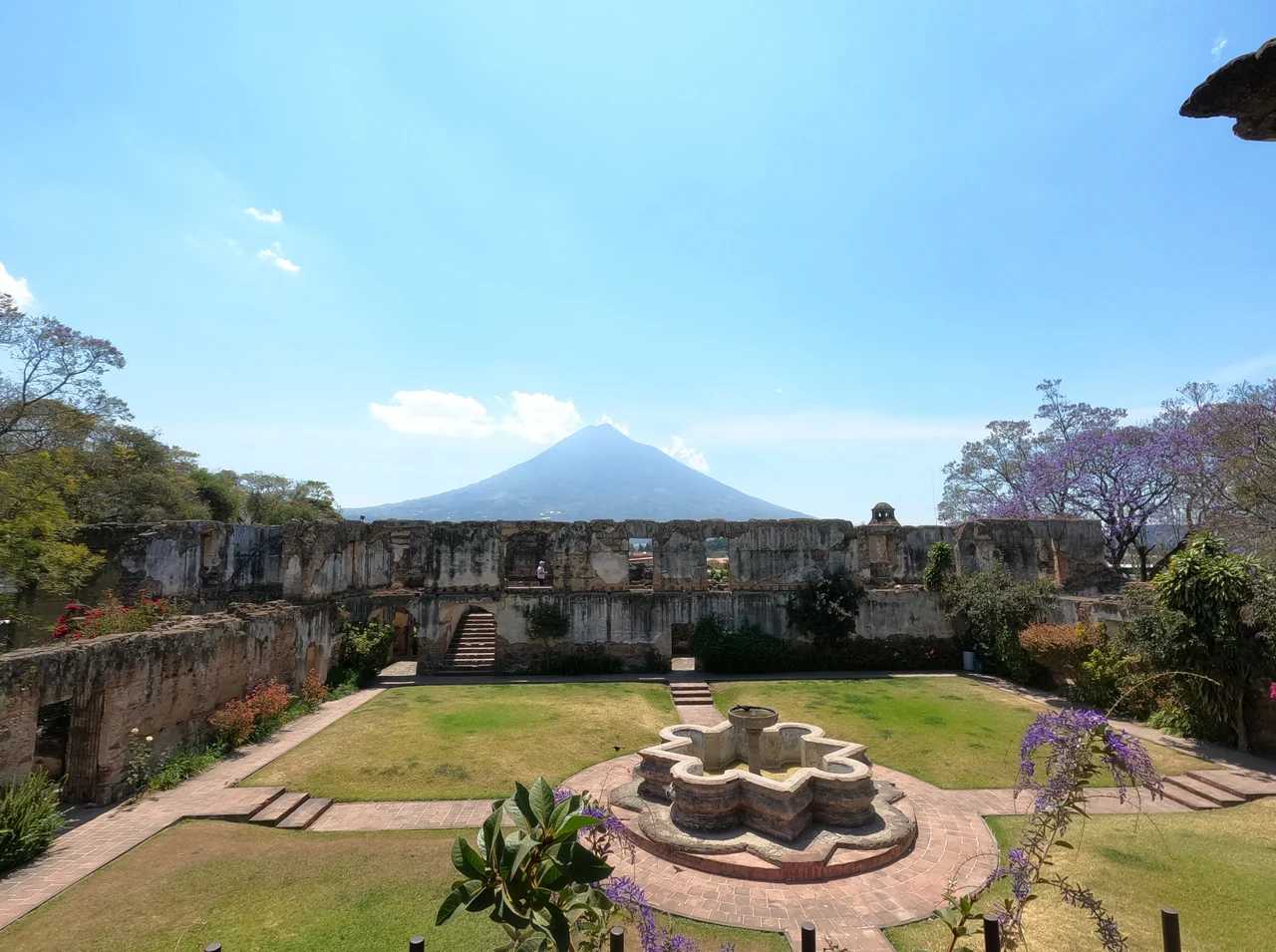 Courtyard, fountain and ruins of the Colegio de San Jerónimo in Antigua, with a volcano in the background.