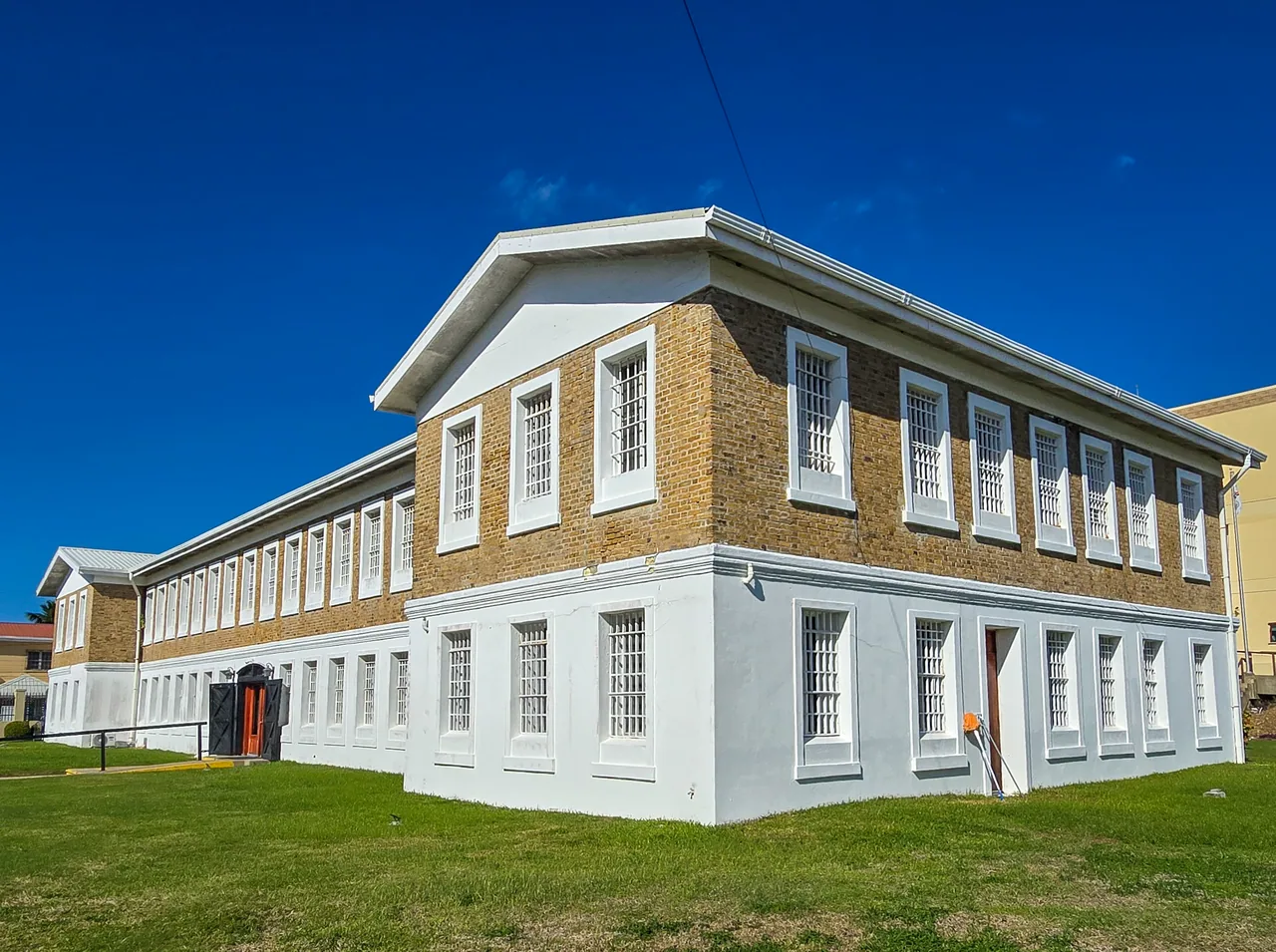 Fachada de ladrillo y planta baja blanca del Museum of Belize, junto al césped.