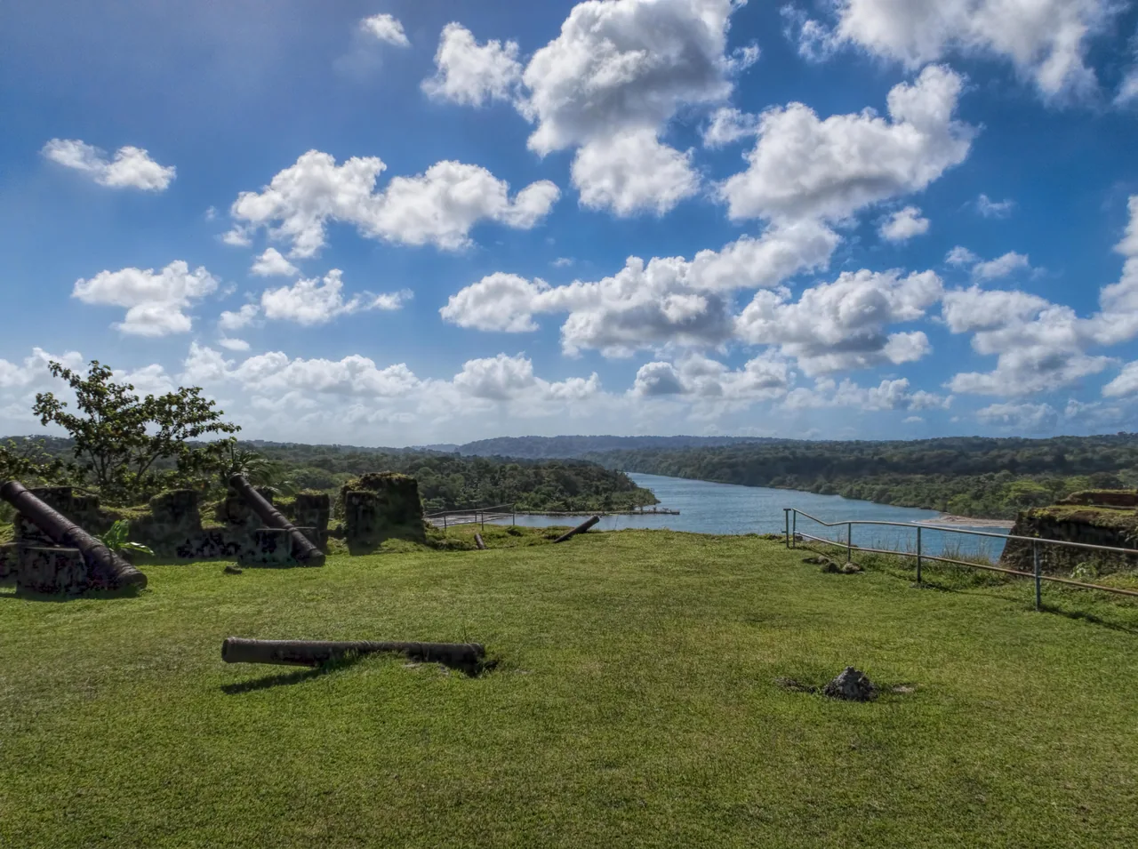 Cannons on the lawn at Fort San Lorenzo and the mouth of the Chagres River between forested hills.