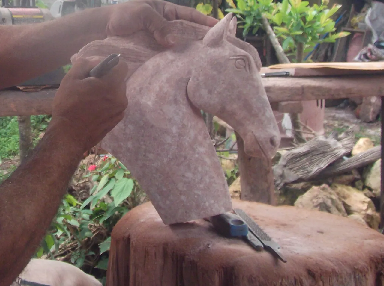 Manos tallando una cabeza de caballo en piedra rosada en un taller.