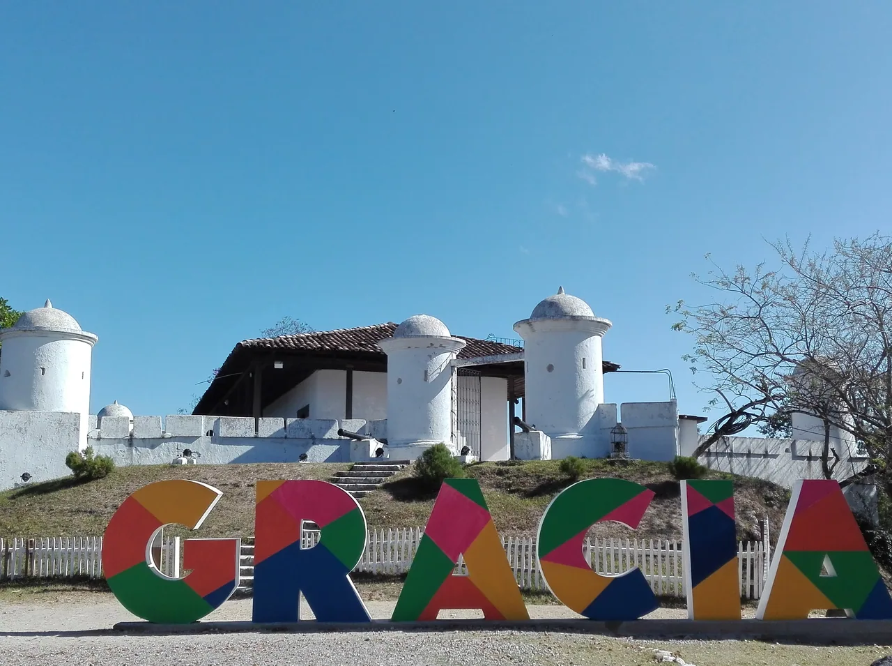 Colourful Gracias letters in front of a white hilltop fort.