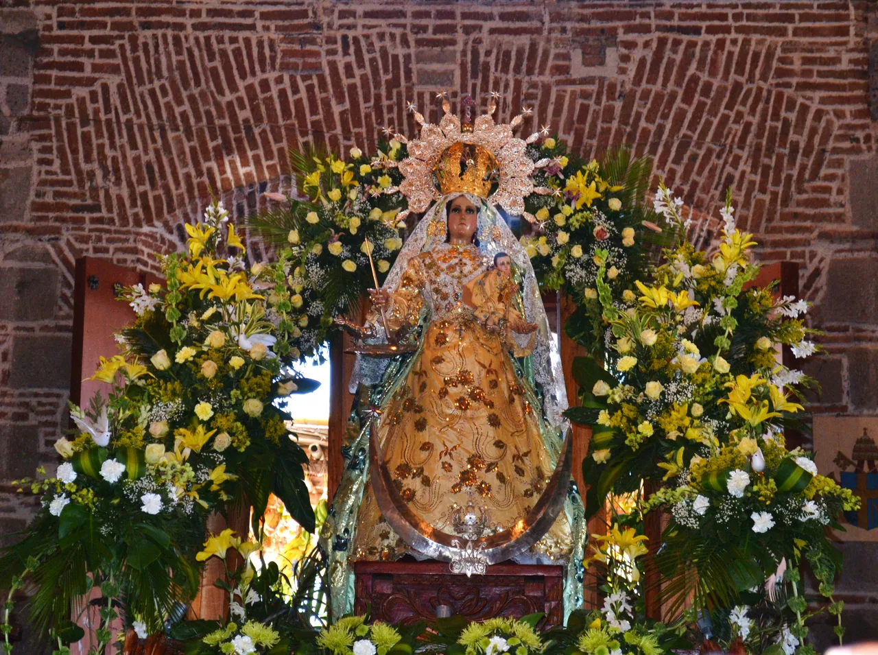 Image of the Virgin of Candelaria in a brick niche with white and yellow flowers.