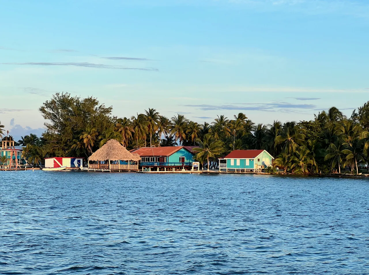 Cayo con palmeras, una palapa y casas de colores, visto desde el agua azul.