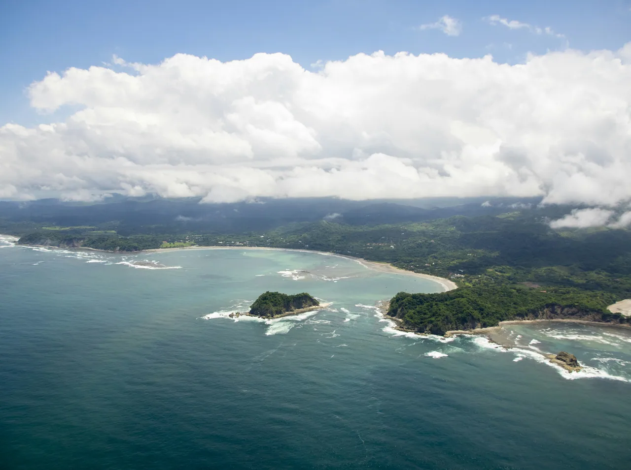 Aerial view of the Sámara coast with an islet and breaking waves.