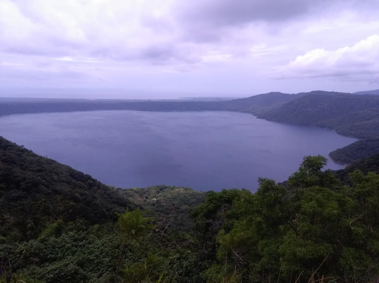 Blue lagoon among wooded slopes, viewed from above beneath mauve clouds.