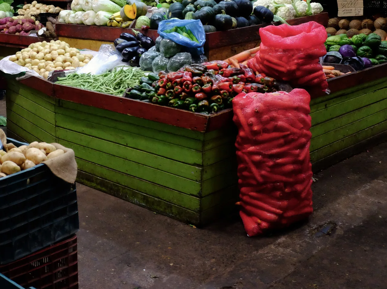 Vegetables piled on a green stall and red sacks at Mercado Borbón.