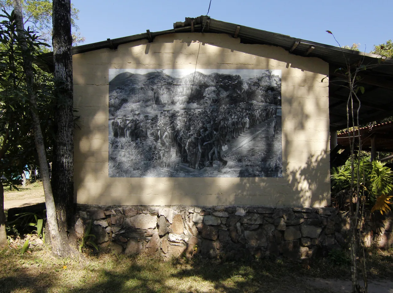 Mural en la pared exterior de un edificio del Museo de la Revolución Salvadoreña, entre árboles.