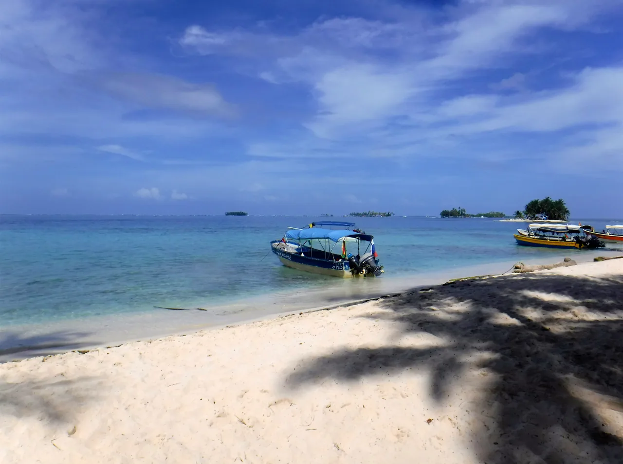 Motorboats beside the white-sand beach of Isla Perro Chico, with palm-tree shadows.