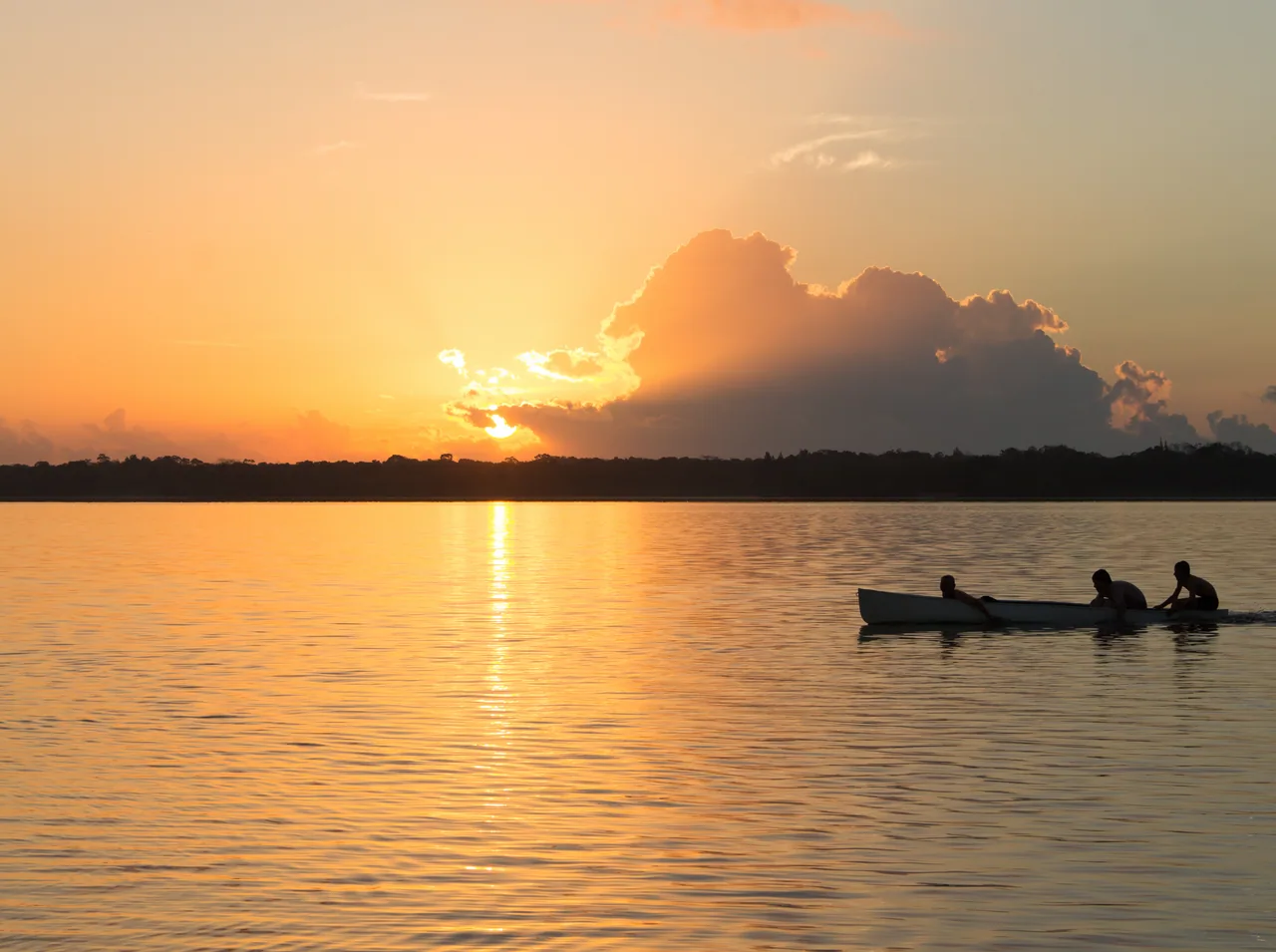 Orange sunrise over a lagoon, with a boat and backlit silhouettes.
