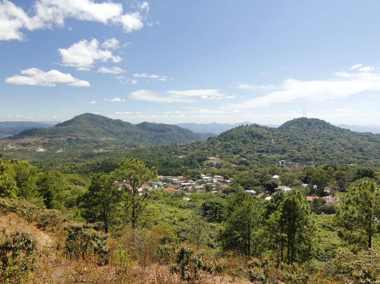 Casas de Perquín entre colinas cubiertas de árboles bajo un cielo azul.