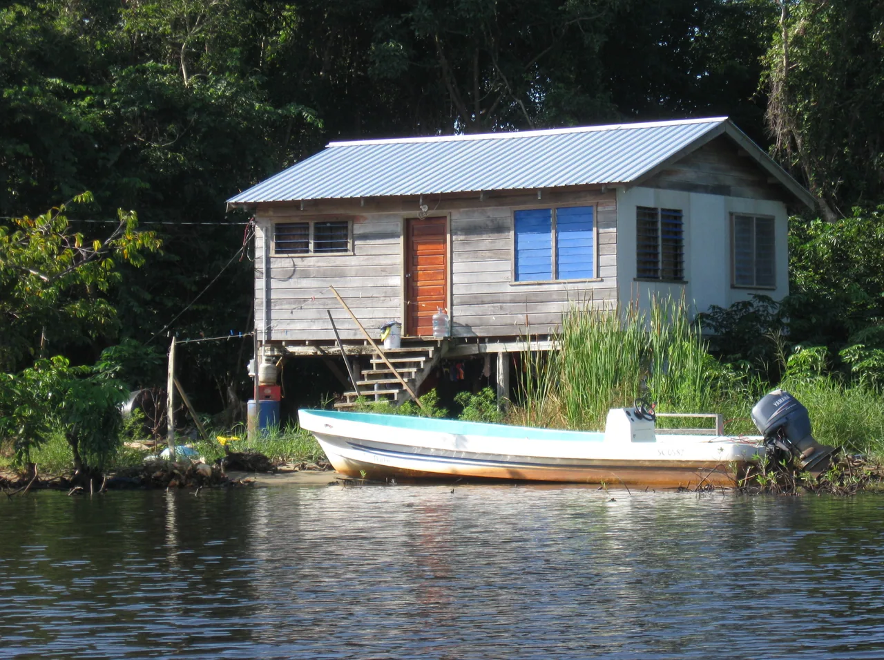 Wooden stilt house beside a river, with a boat moored in front.