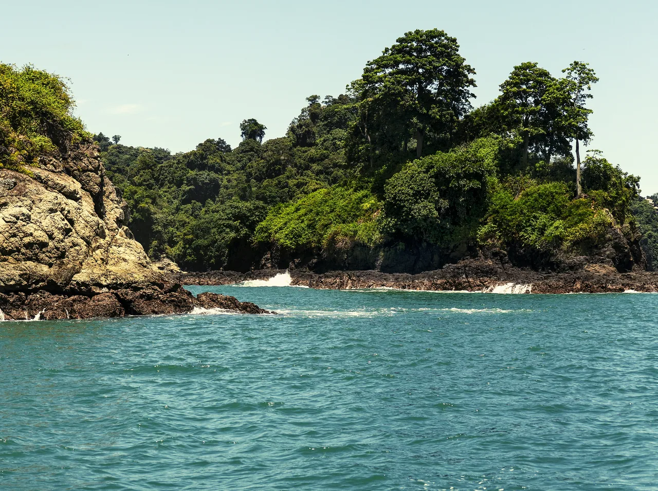 Vegetation-covered rocks and turquoise water beside Playa Biesanz.