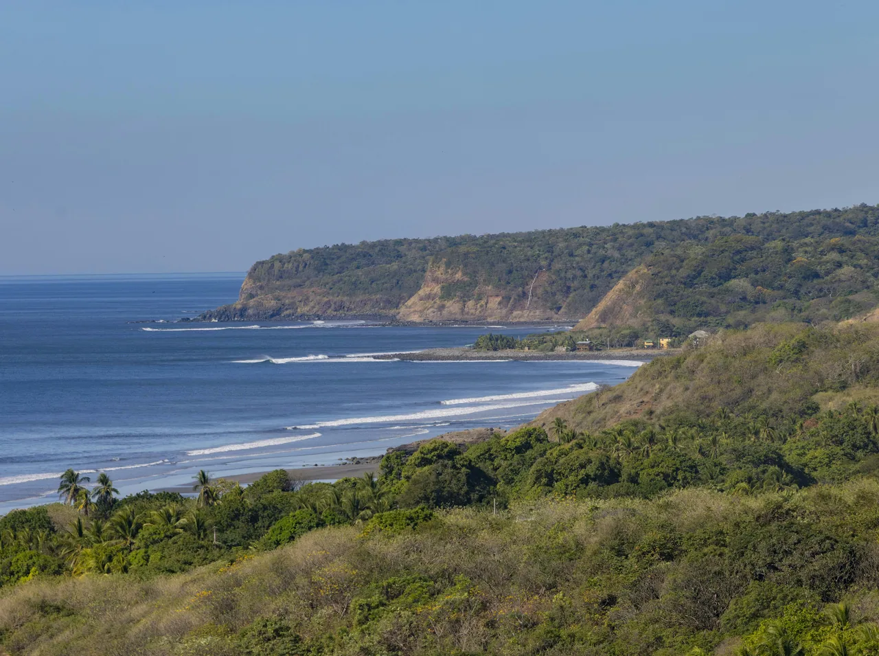 Olas en Playa Las Flores, junto a una punta de acantilados y vegetación.