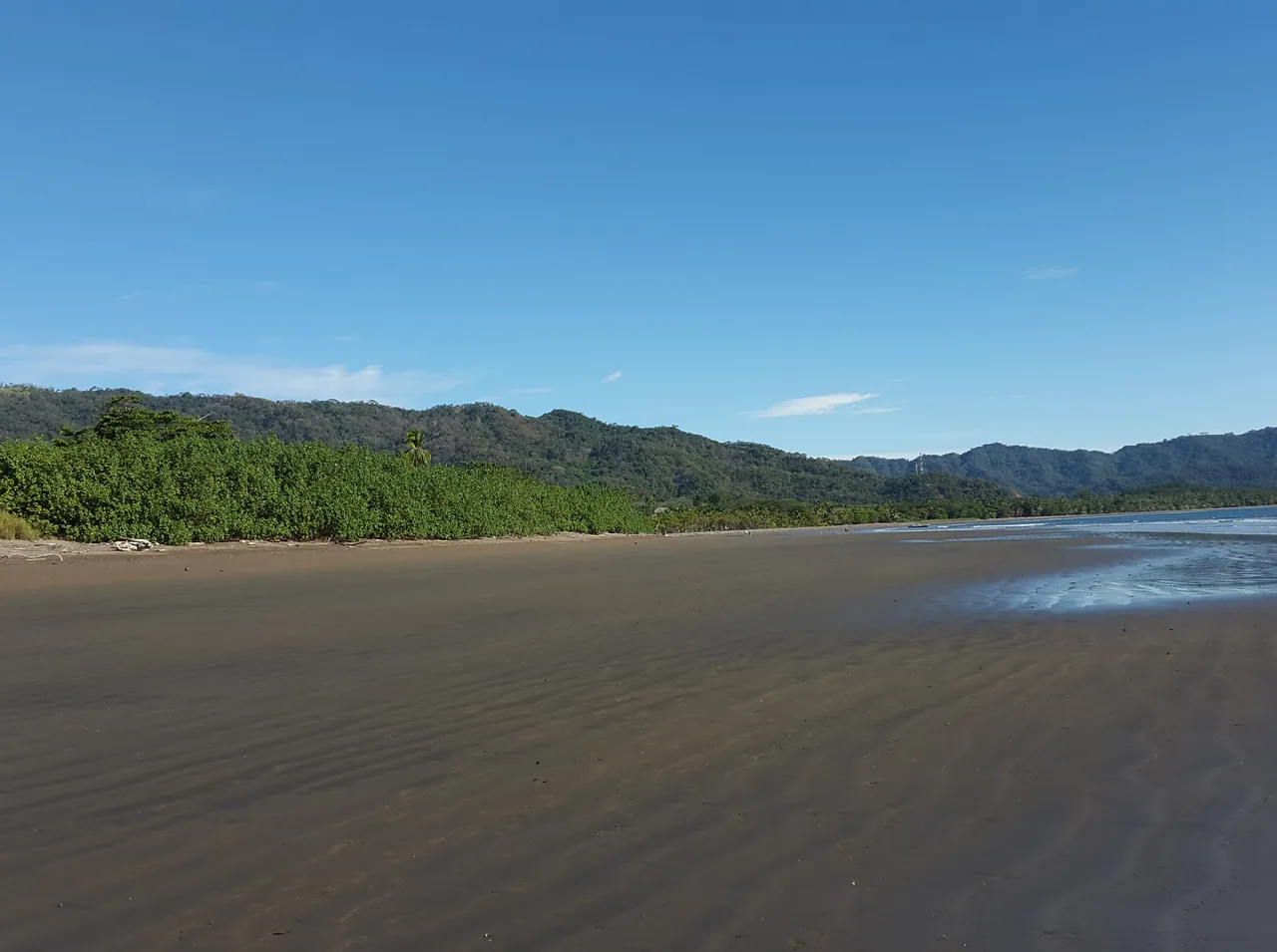 Wet sand and coastal hills at Tambor Beach.