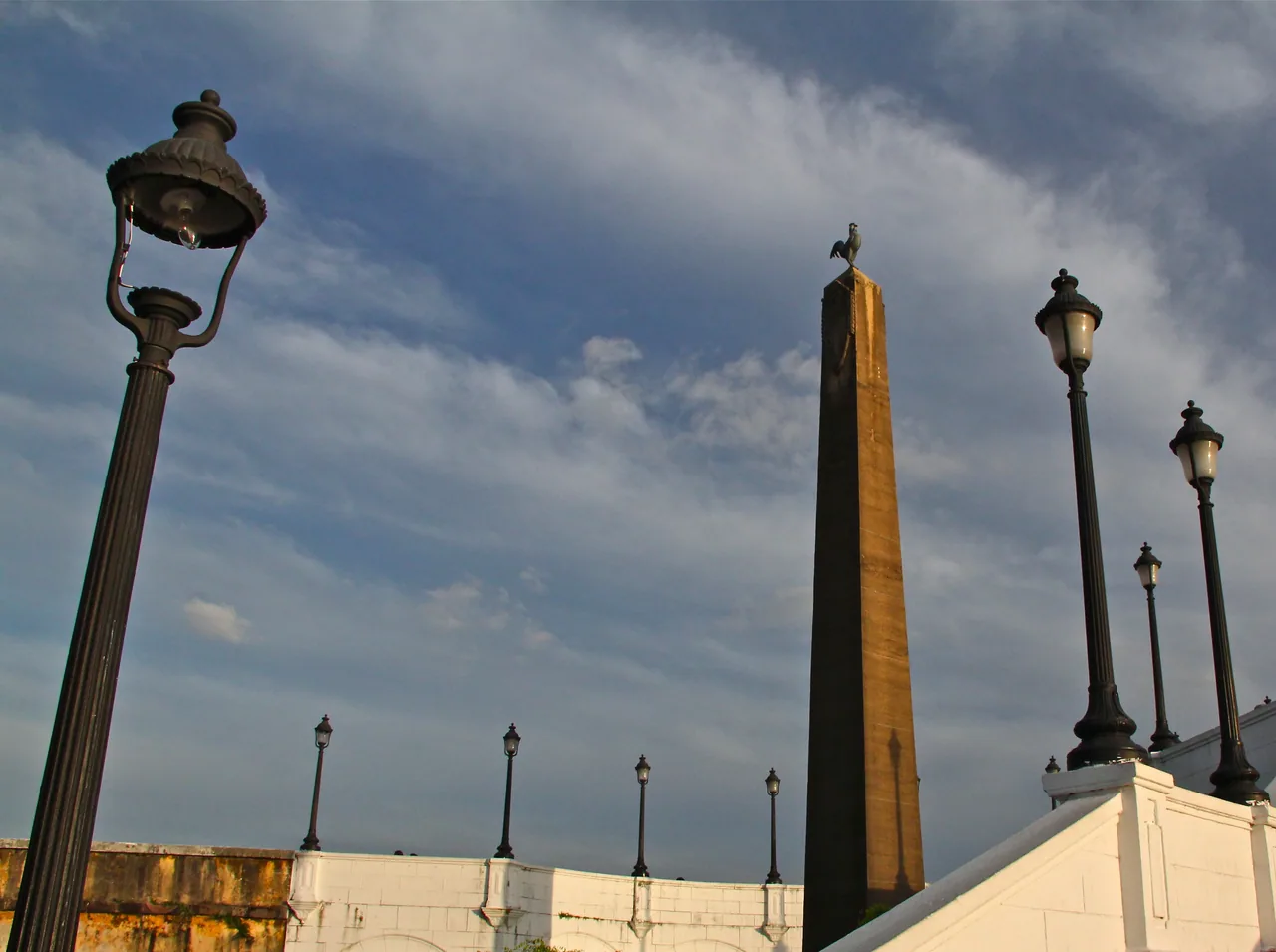 Obelisco de la Plaza de Francia entre farolas y muros blancos bajo un cielo con nubes.