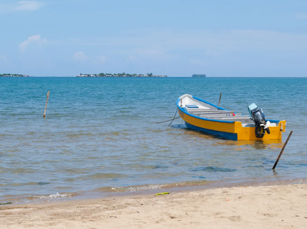 A yellow and blue motorboat moored by the shore, with the Cartí islands in the background.
