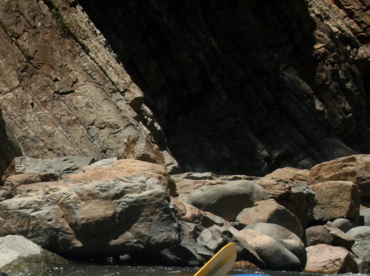 A rock wall and water of the Naranjo River at El Chorro, with part of a paddle at the edge.