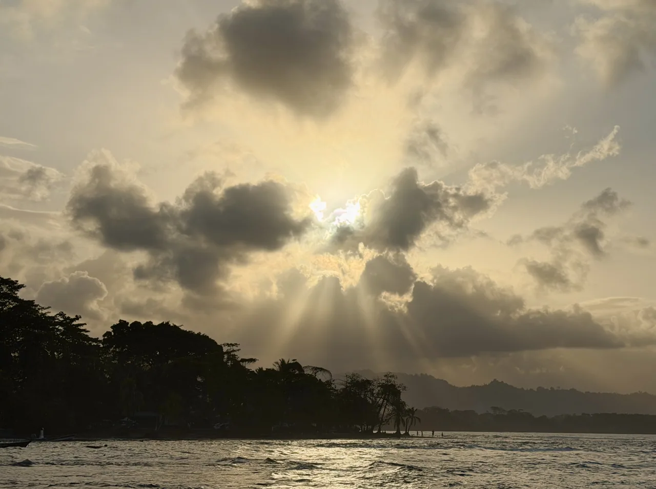 Sunbeams through clouds over the sea and Puerto Viejo coastline at sunset.