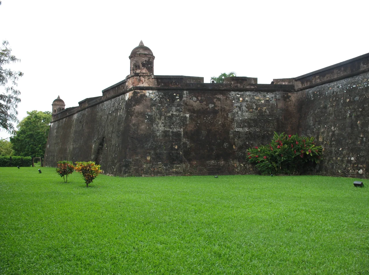 Stone fort wall and sentry turret above a green lawn.