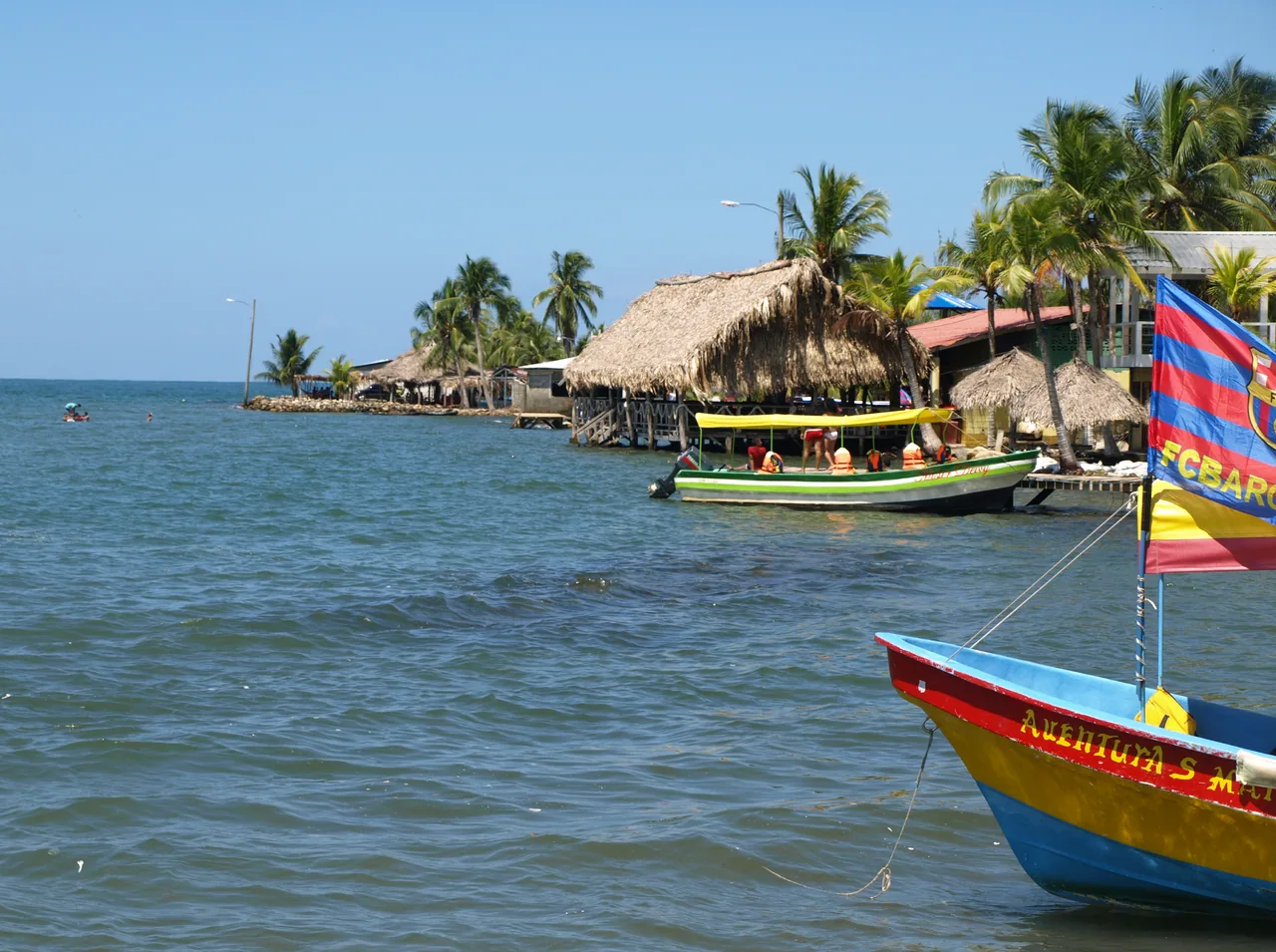 Boats beside thatched-roof restaurants over calm sea water.