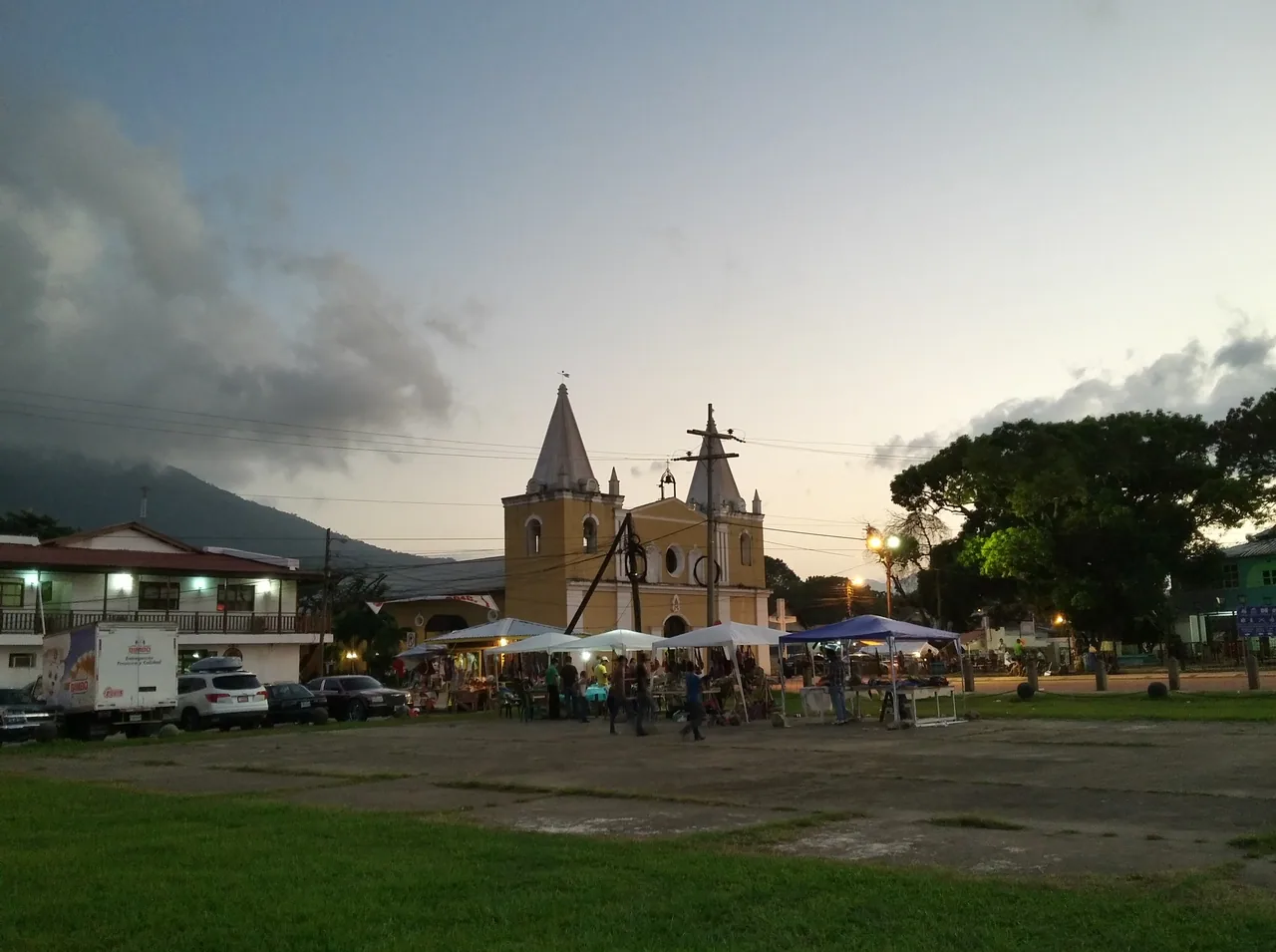 Canopied stalls and a cathedral behind a grassy square at dusk.
