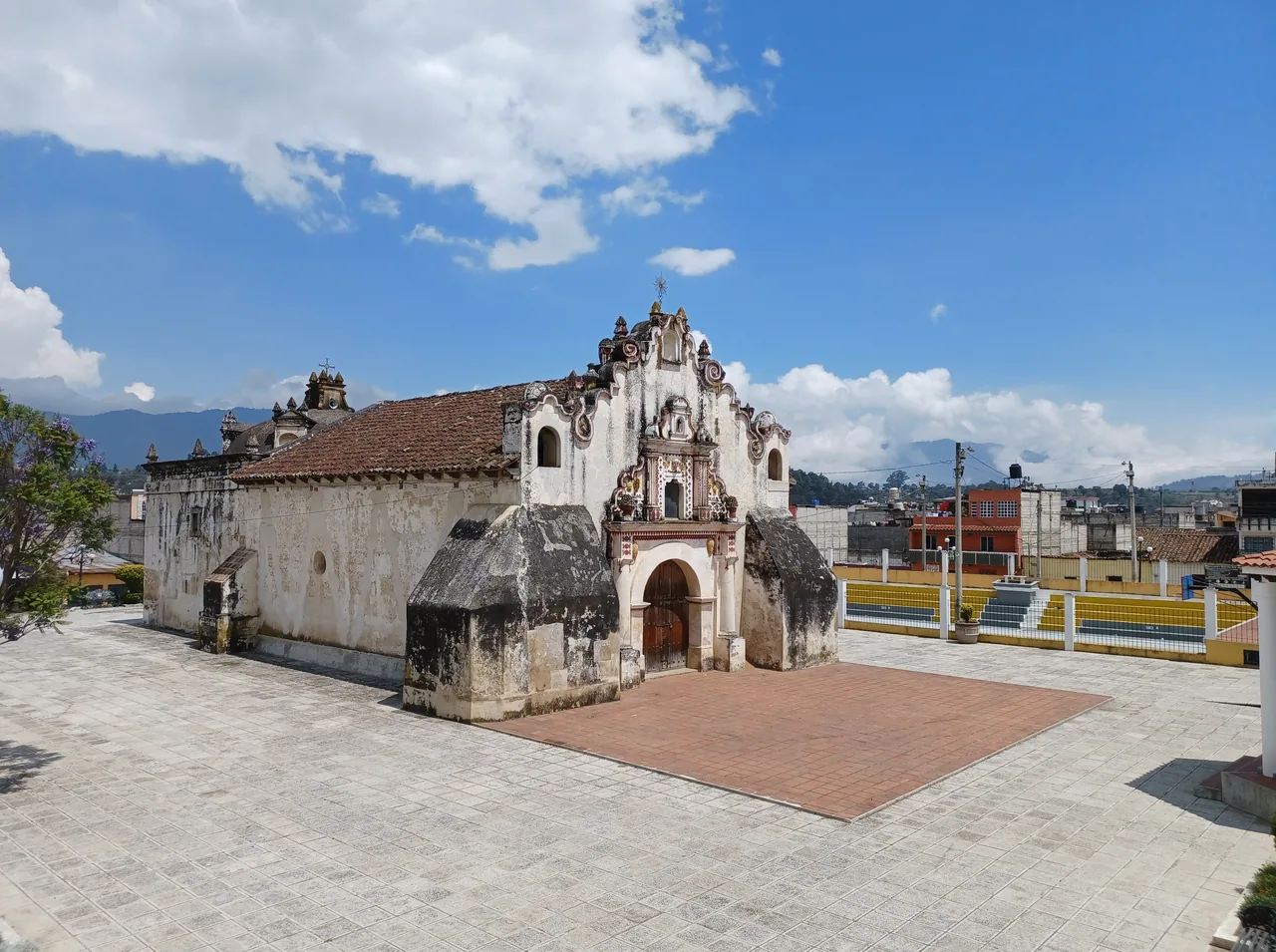 White chapel with a tiled roof and bell gable beside a paved square.